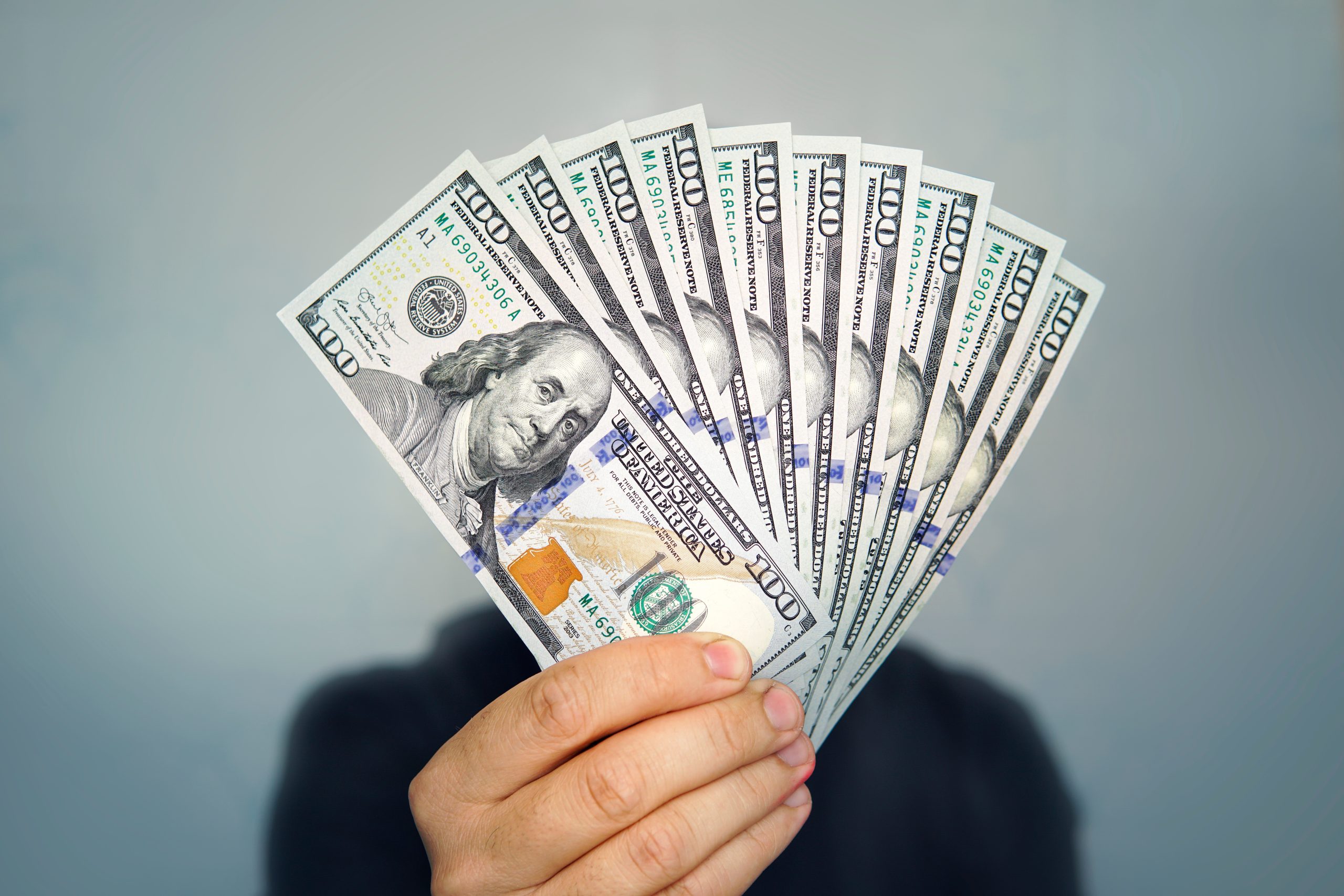 Person holding a fan of US hundred-dollar bills, close up of the cash