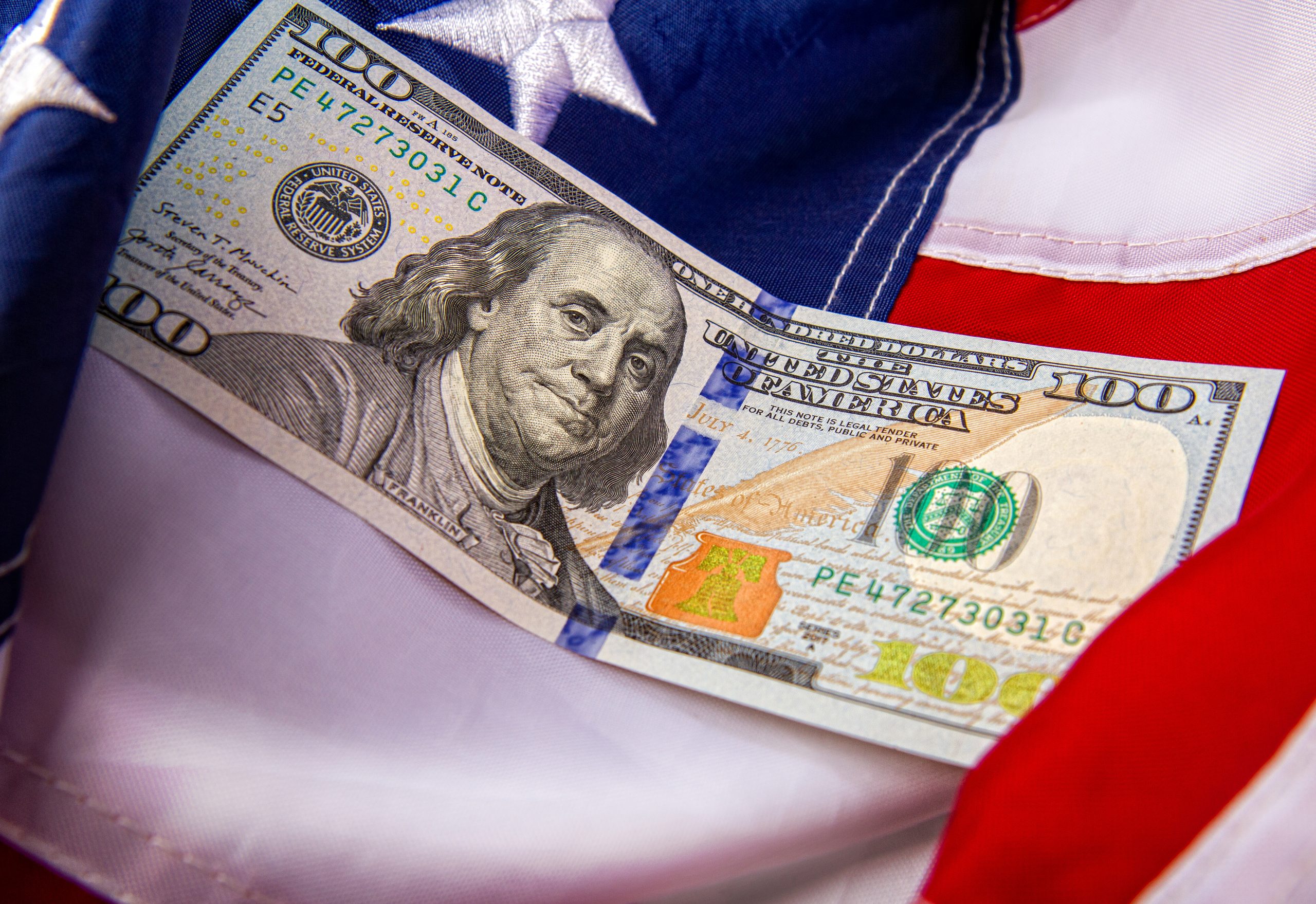 Close-up of US hundred-dollar bills laid on a folded American flag.