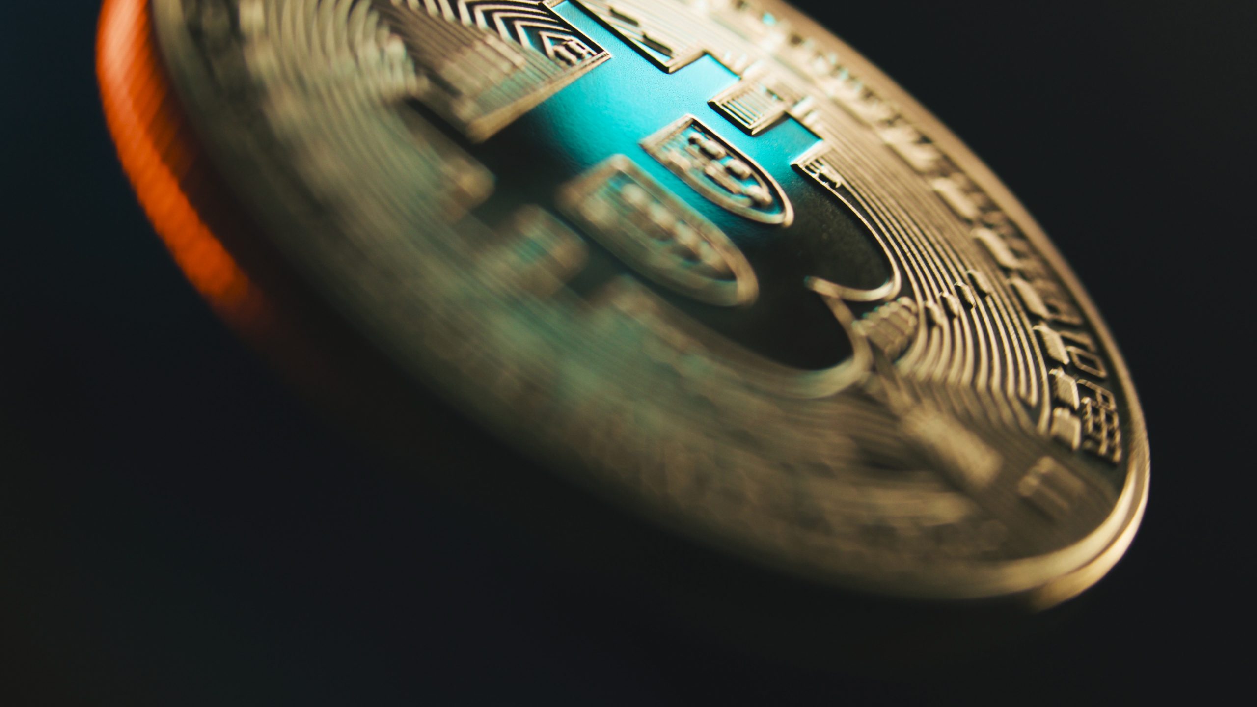 Close-up of a metallic cryptocurrency coin with intricate circuitry patterns and a blue-green hue, set against a dark background.