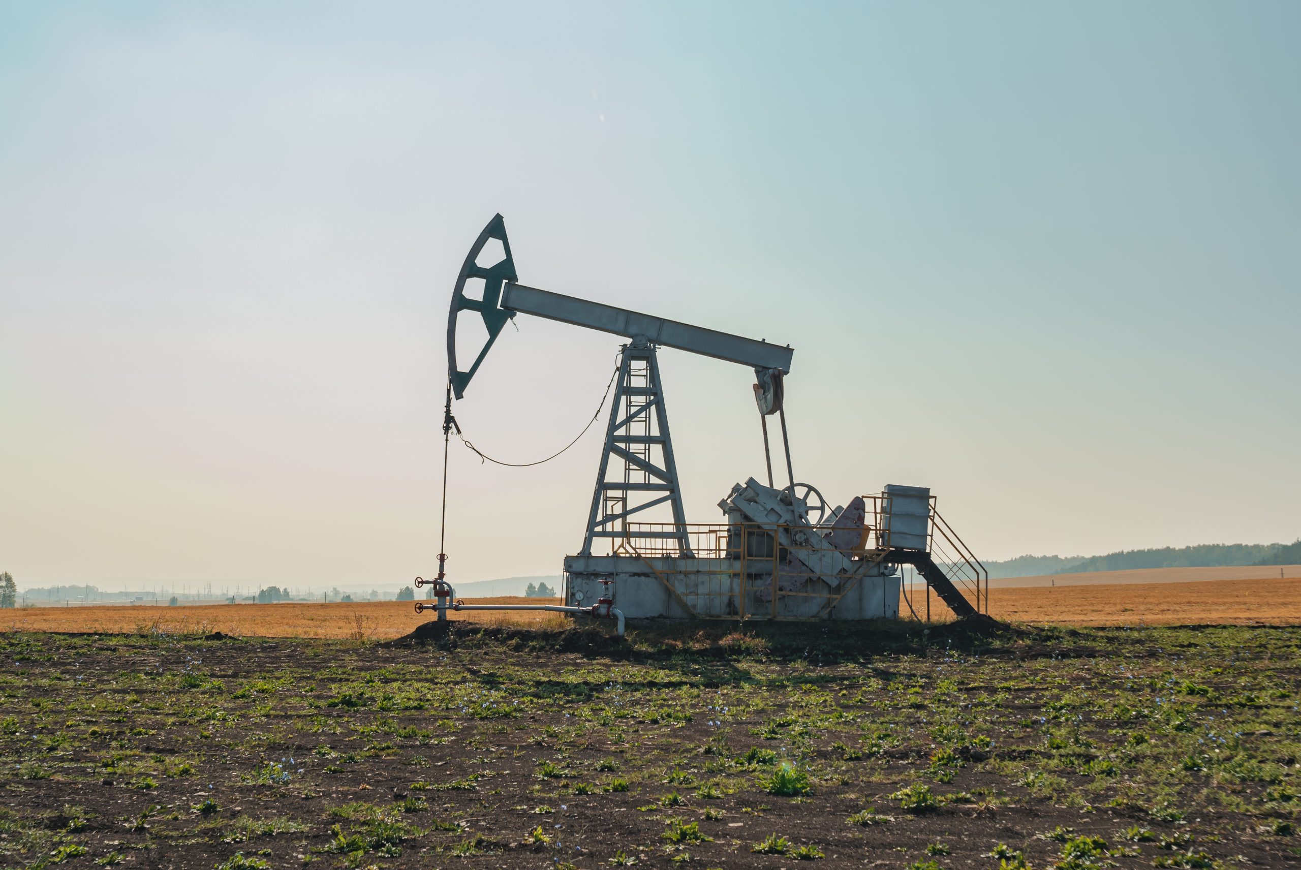 Oil pumpjack pumping oil in a flat, open field under a clear sky, with distant horizon.