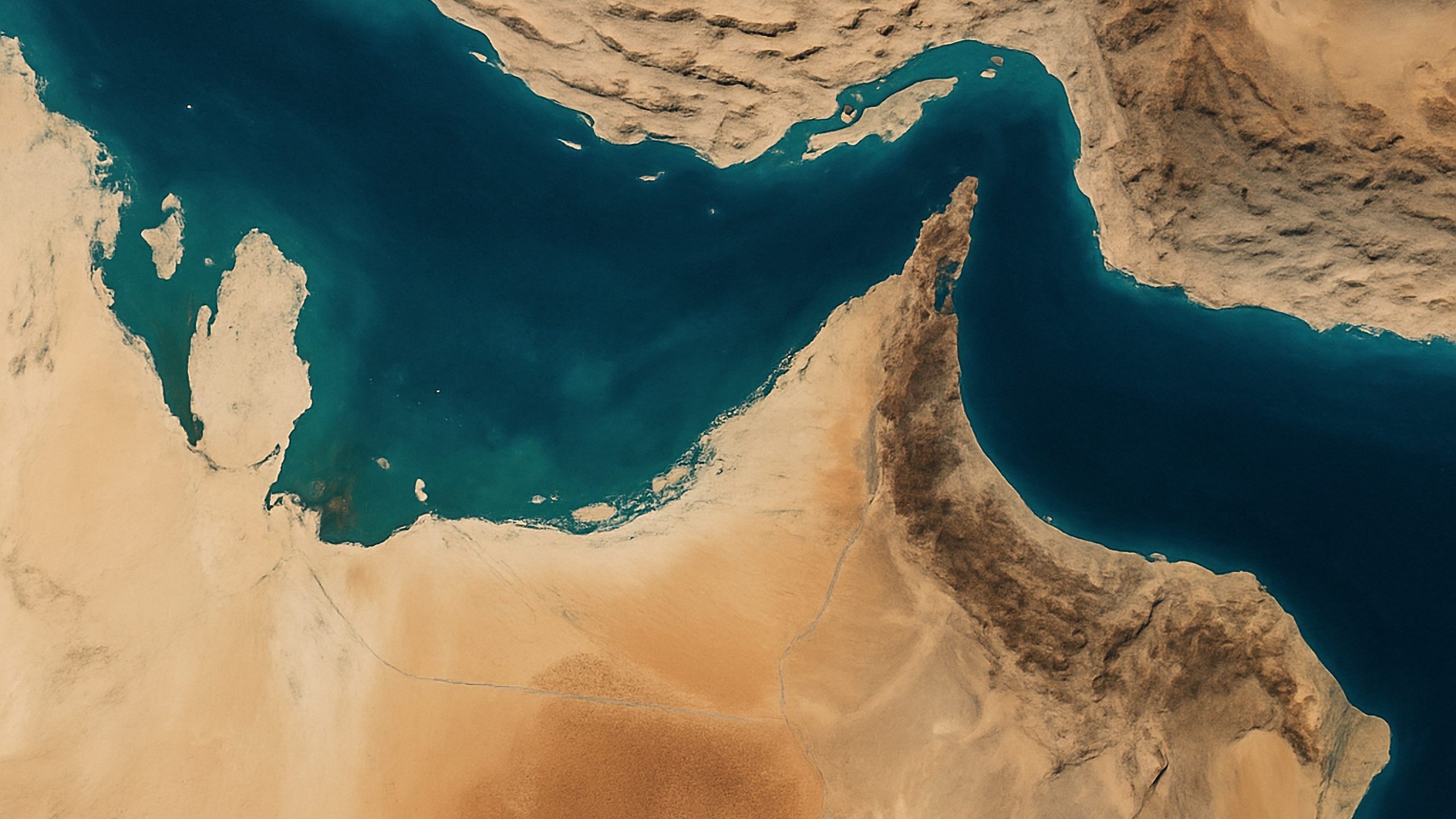 Aerial view of a turquoise coastal inlet surrounded by sandy tan terrain and rugged cliffs coast.