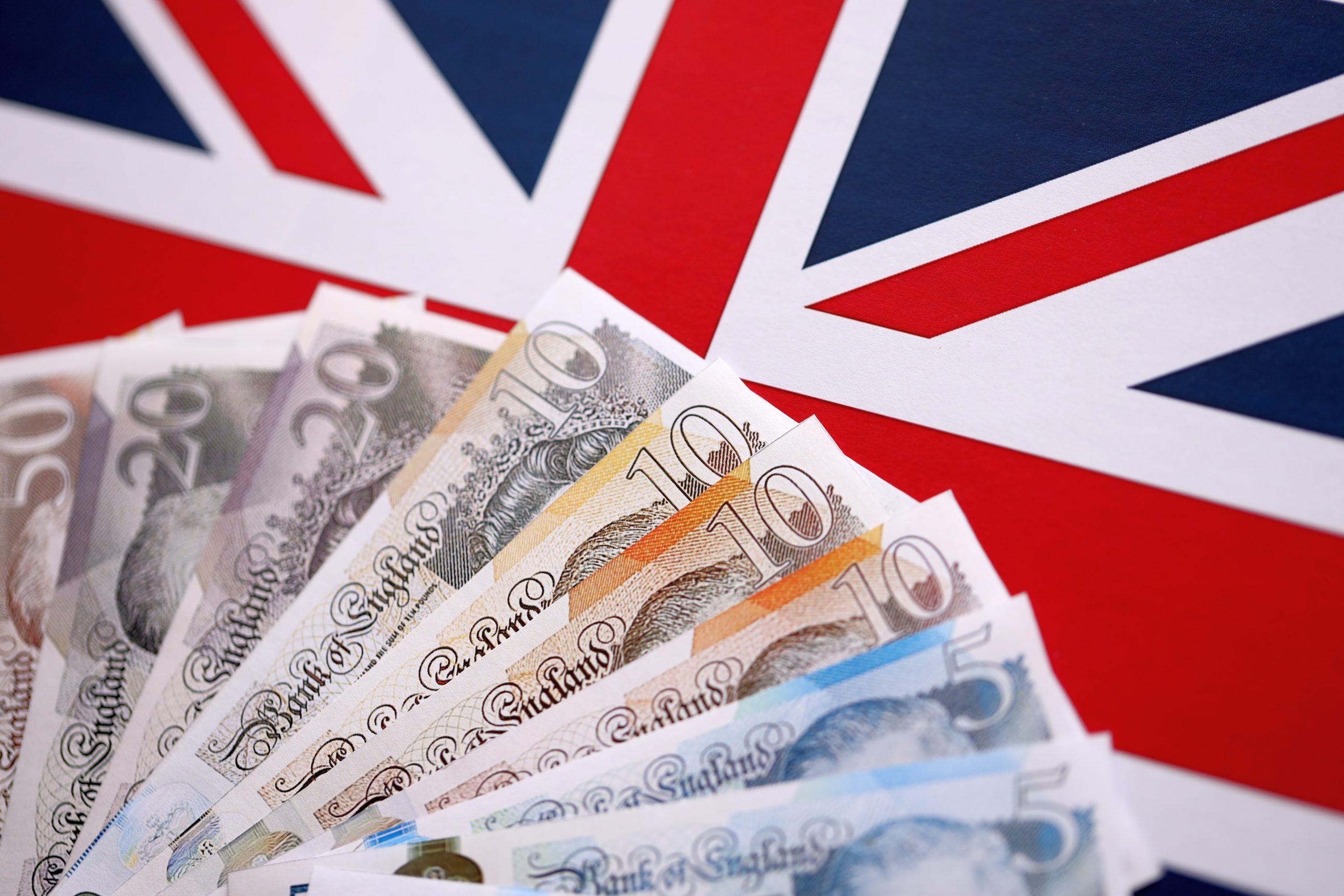 Fanned UK banknotes spread over a Union Jack background, suggesting money and national finance.
